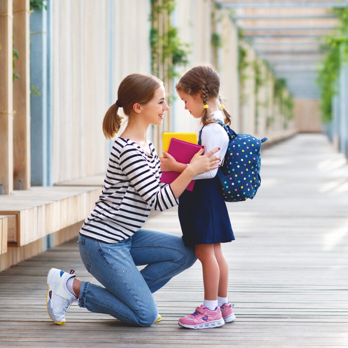 mother kneeling down and looking at daughter in school uniform 